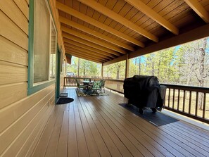 Eine überdachte Veranda mit Holzterrasse, Grill und Blick ins Grüne.