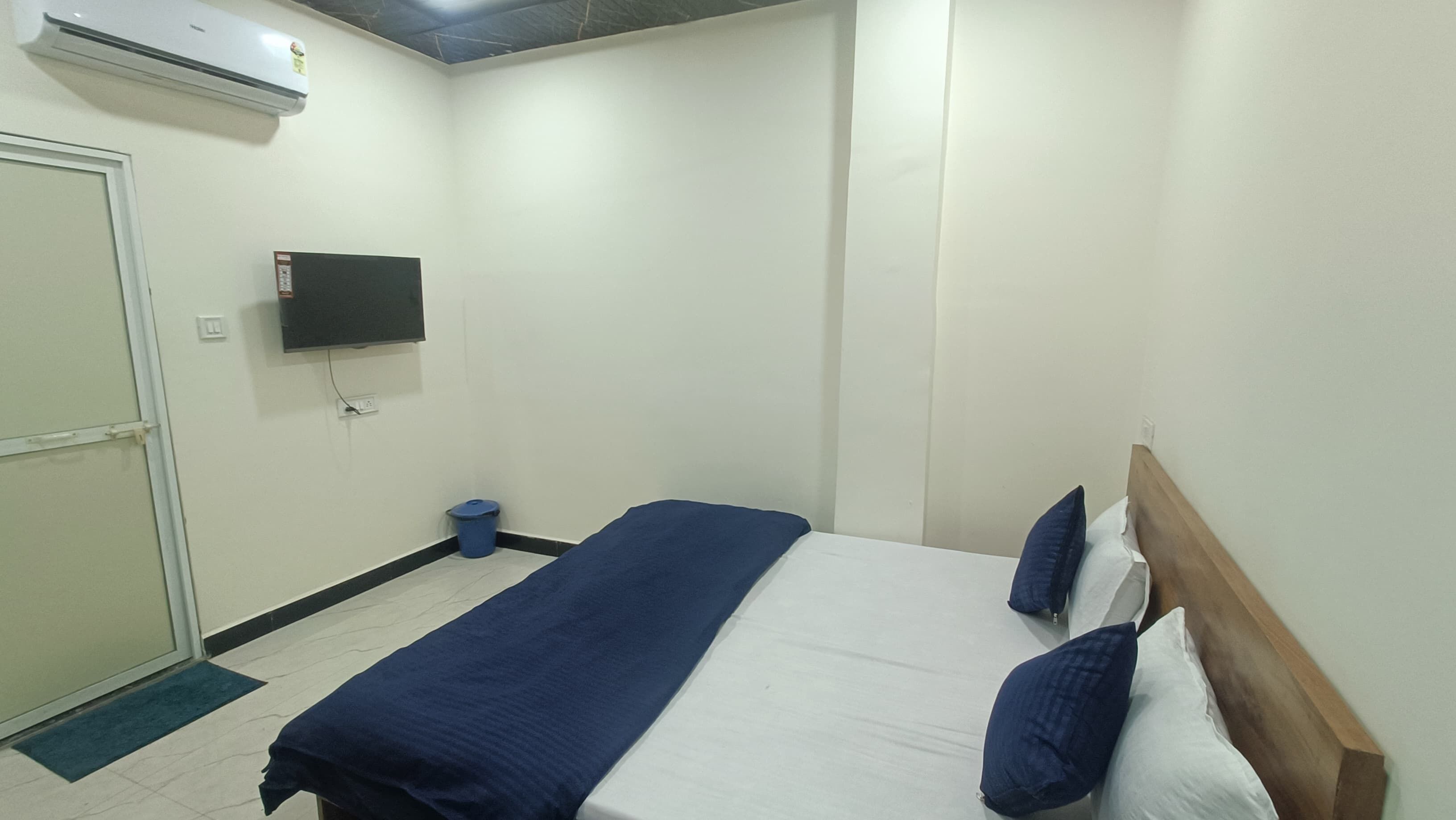 A bedroom with a bed, a TV mounted on the wall, and a door.