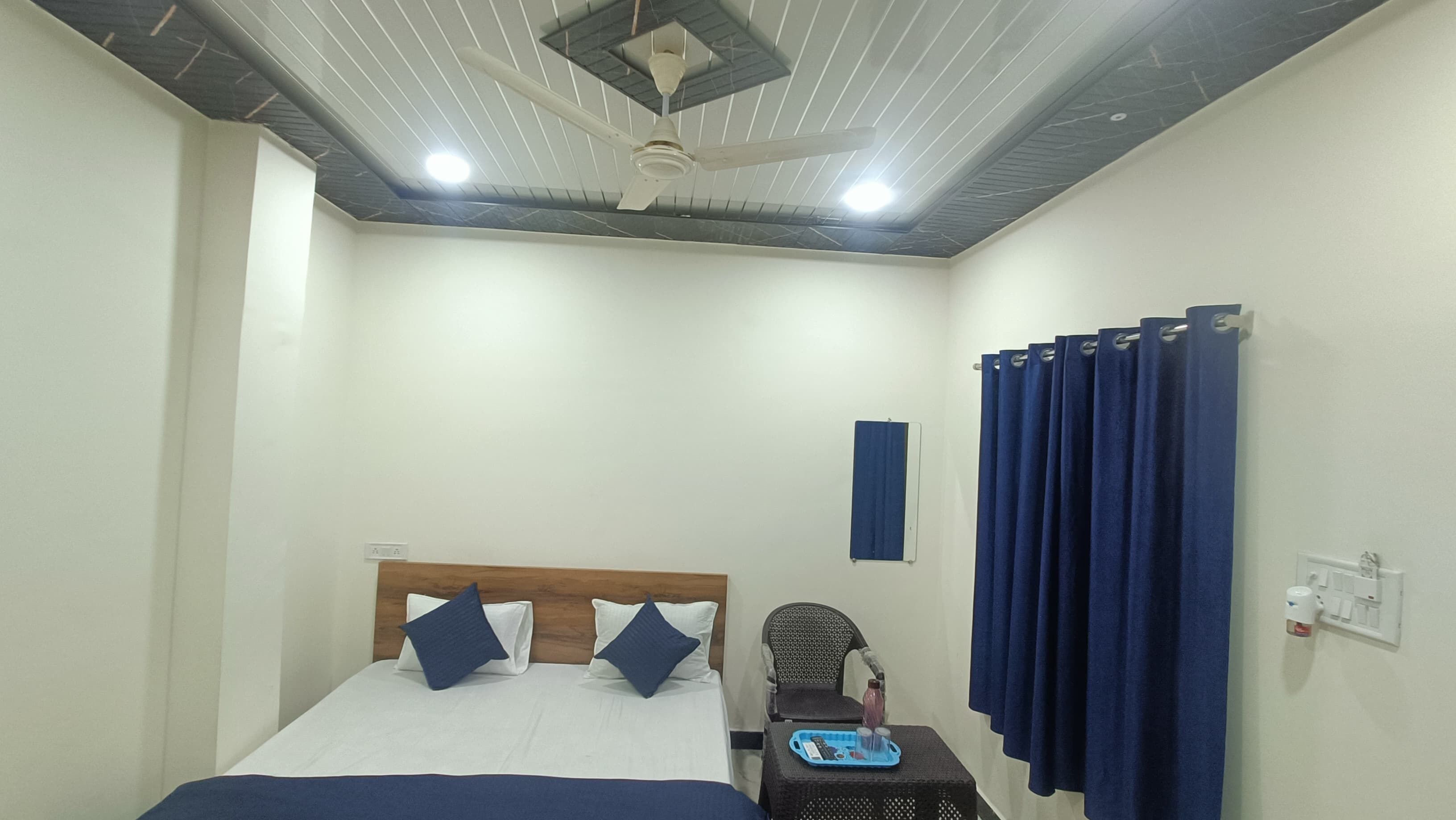 A bedroom with a bed, a chair, a table with a tray, a ceiling fan, and a curtain.