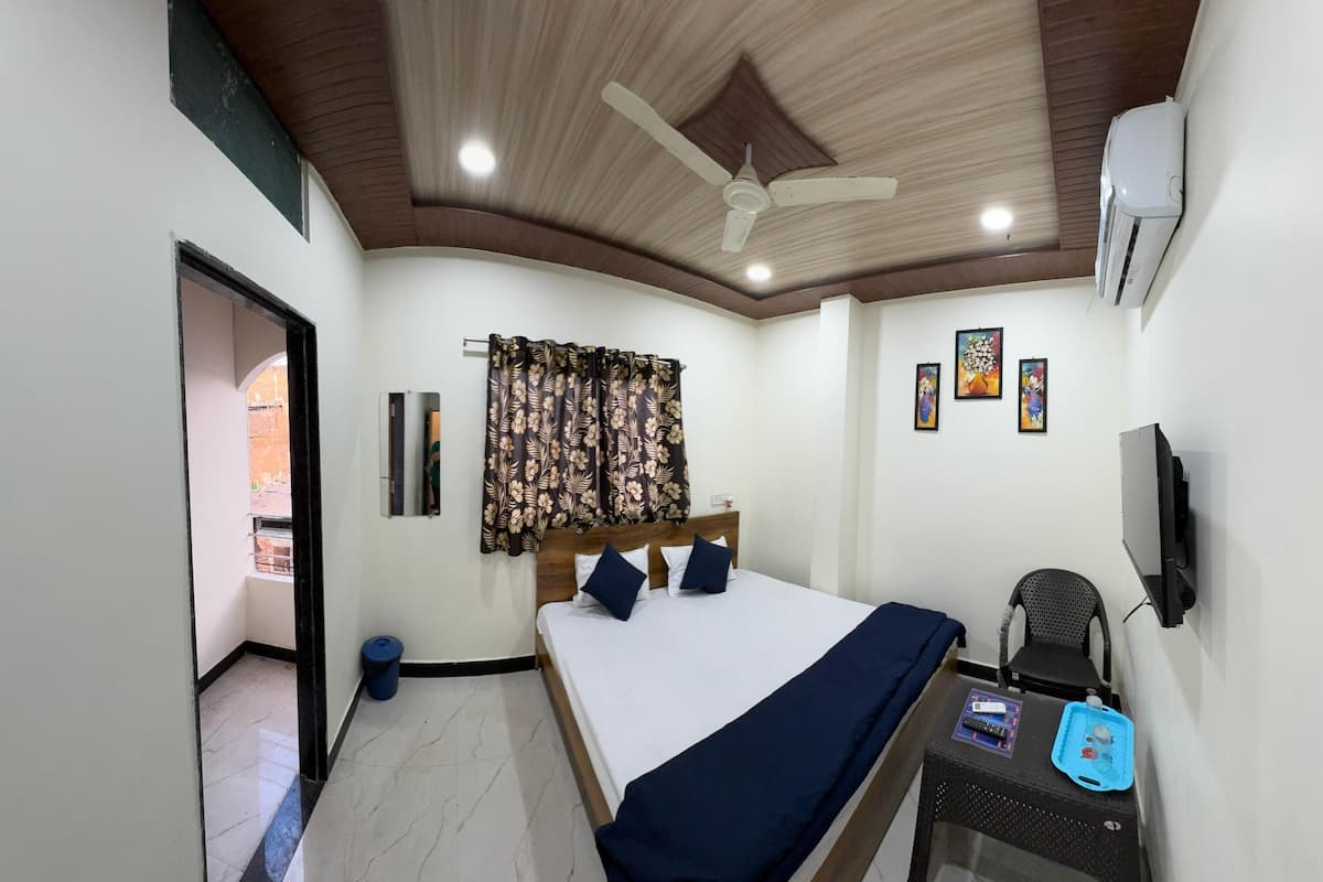 A bedroom with a bed, a desk, a chair, a ceiling fan, and a wall-mounted TV.