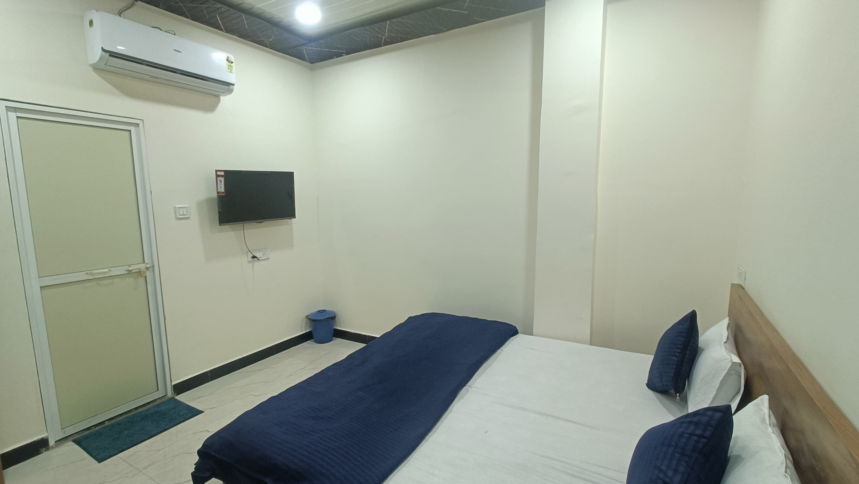 A hotel room with a bed, a television mounted on the wall, a door, and an air conditioning unit.