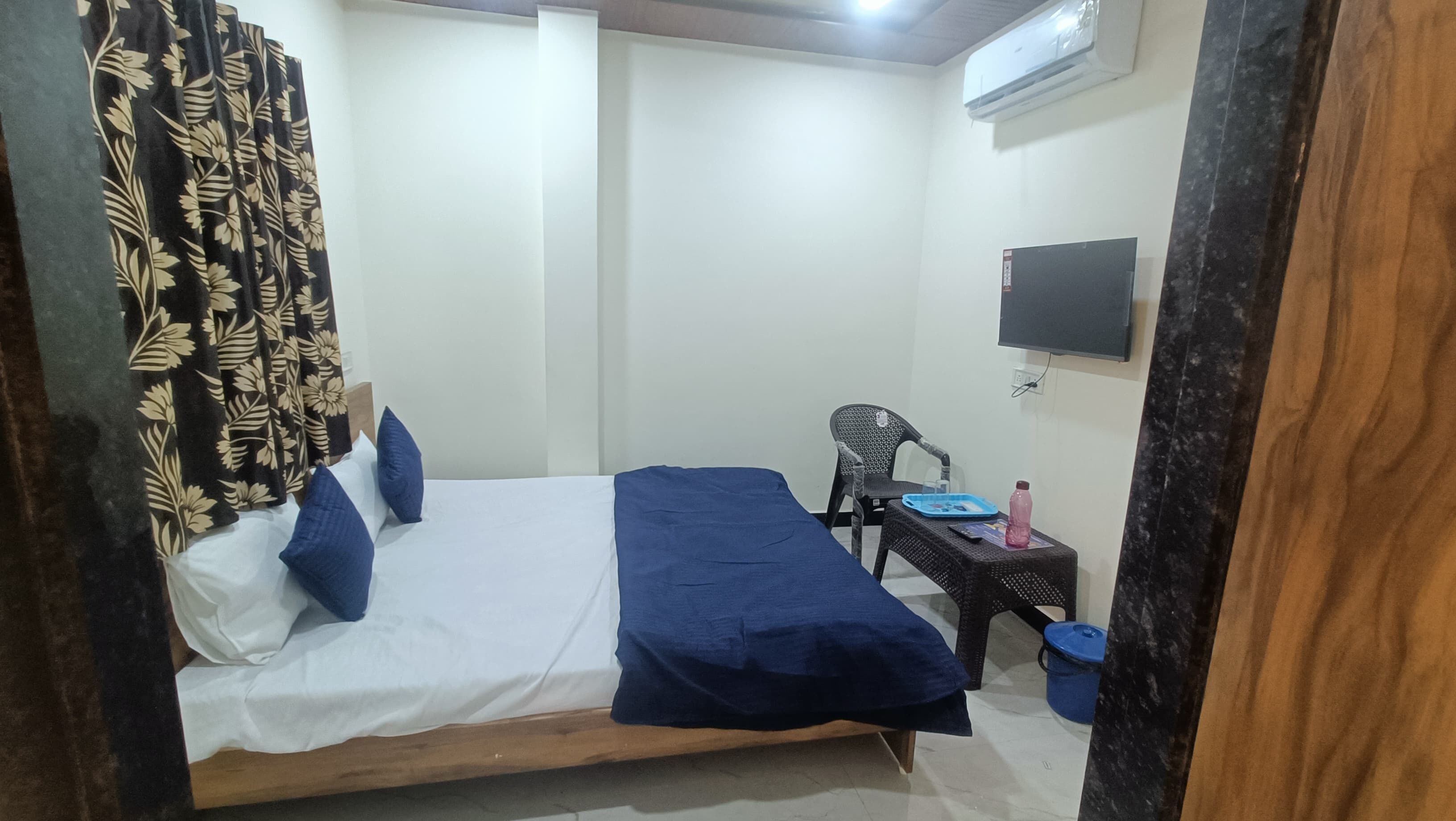A room with a bed, a chair, a small table, an air conditioner, and a TV.