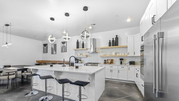 A modern kitchen with a central island, bar stools, stainless steel appliances, and pendant lighting.
