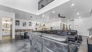 A spacious living area with a large leather sectional sofa, a kitchen in the background, and a staircase leading to an upper level.
