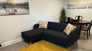 Una sala de estar con un sofá seccional, un felpudo amarillo y una zona de comedor con una mesa y sillas.