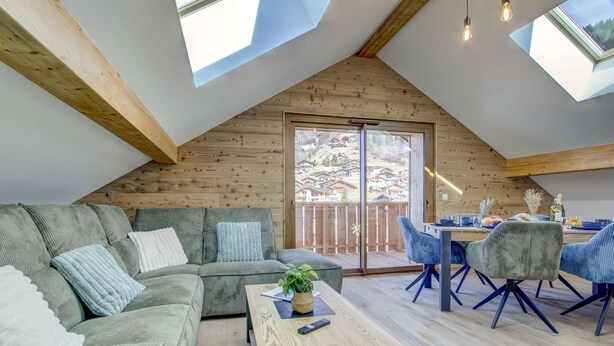 A cozy room with a sloped ceiling, wooden walls, a sofa, a coffee table, and a dining area with chairs.