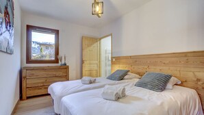 A bedroom with two beds, wooden headboard, a wooden dresser, a window with a view, and a hanging light fixture.