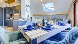 A modern kitchen with dark cabinets, a wooden ceiling, and a dining area with blue upholstered chairs and a wooden table set for four.
