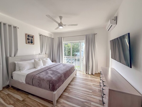 A modern bedroom with a bed, ceiling fan, and a TV mounted on the wall.
