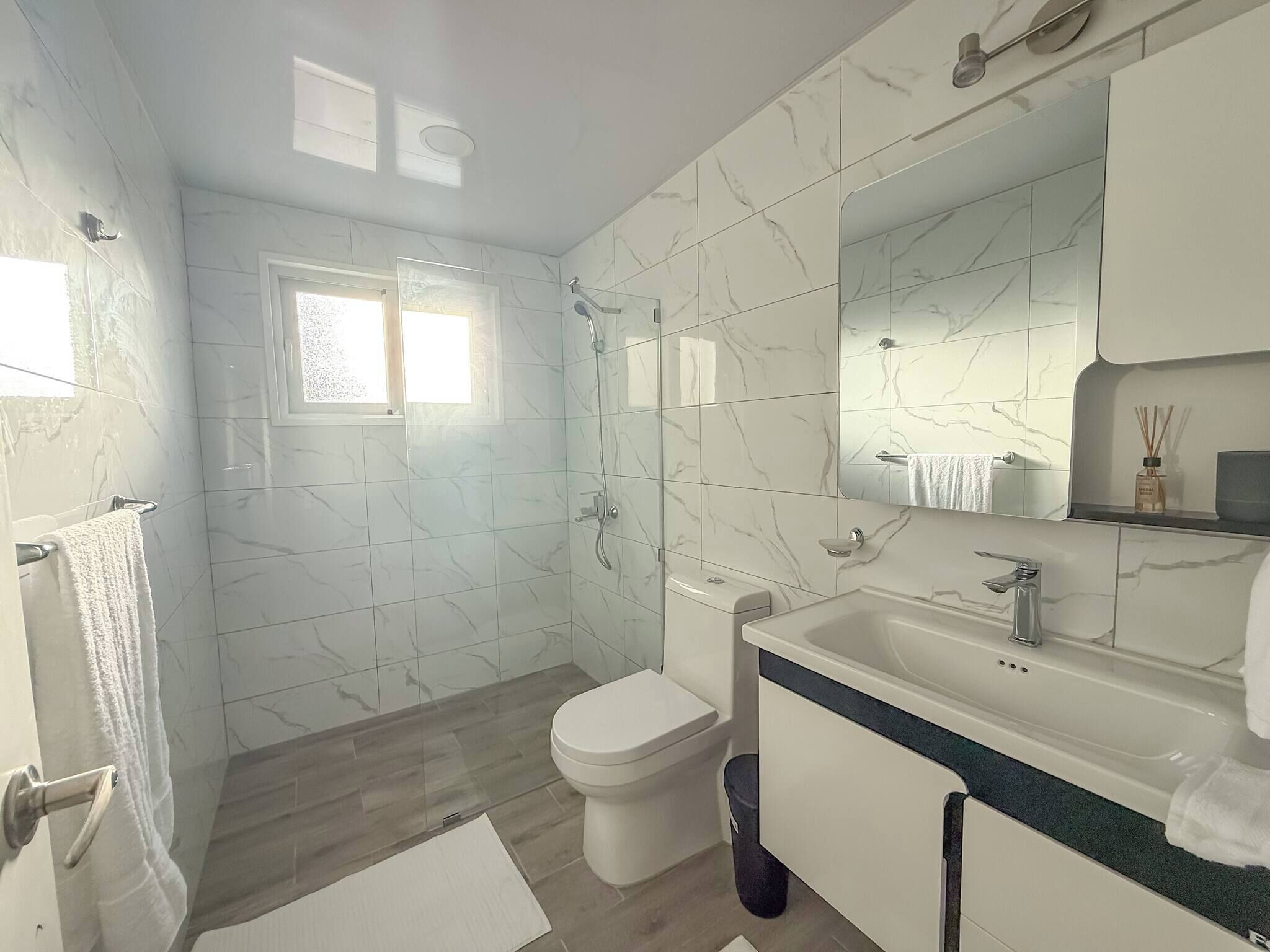Ein modernes Badezimmer mit Marmorfliesen, einer Toilette, einer Dusche und einem Waschbecken mit Spiegel darüber.