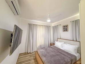 A bedroom with a bed, curtains, a ceiling fan, and a mounted TV.