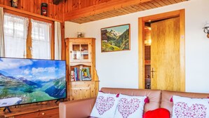 Una sala de estar acogedora con un sofá de cuero, un televisor de pantalla plana, estanterías de madera y una pintura de montañas.
