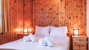 Una habitación con paneles de madera, una cama, dos mesitas de noche y un buró.