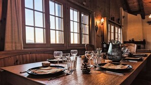 Una larga mesa de madera dispuesta para comer, con múltiples copas de vino, platos y cubiertos.