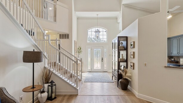 A spacious foyer with a grand staircase, a large window, and a decorative cabinet.