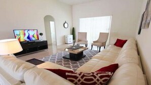 Een moderne woonkamer met een beige bank, een salontafel en twee fauteuils. Achterin staat een televisie en een klein kastje.