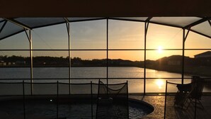 Ein überdachter Außenbereich mit Pool, Sitzgelegenheiten und Blick auf den Sonnenuntergang über dem Wasser.