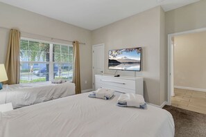 A hotel room with two beds, a TV on the wall, a dresser, and a window with curtains. - Amazing 4BDR w/ pool near Disney - 4914 (Kissimmee)