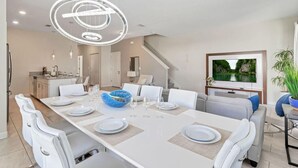 A modern dining area with a long table, white chairs, and a blue bowl centerpiece.