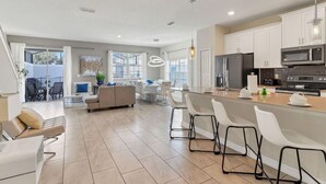A modern kitchen with white cabinets, a central island with bar stools, and a dining area with a sofa and chairs.