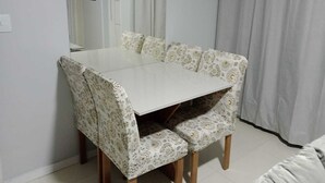 A dining area with a white table and patterned chairs, a white wall, and a door with a picture frame. - Casa do Naldo Hospedaria Aju - Cozy apartment for family vacations. (Jabotiana Aracaju)