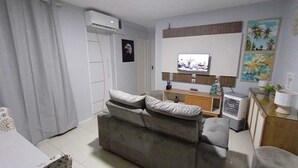 A living room with a grey sofa, a TV on the wall, and a small cabinet. - Casa do Naldo Hospedaria Aju - Cozy apartment for family vacations. (Jabotiana Aracaju)