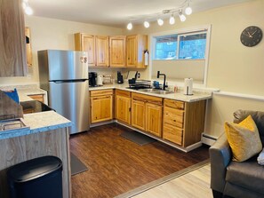 A compact kitchen with wooden cabinets, a stainless steel refrigerator, a built-in oven, and a window with blinds.