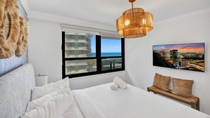 A hotel room with a bed, a large window with a cityscape view, a hanging light fixture, and a wall-mounted painting. - Chic Coastal Getaway Steps to the Beach with Resort Amenities, Pools, Sauna & Gym 708 (Miami Beach)