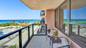 A balcony with a view of the beach and ocean, a seating area with a table and chairs, and a potted plant. - Chic Coastal Getaway Steps to the Beach with Resort Amenities, Pools, Sauna & Gym 708 (Miami Beach)