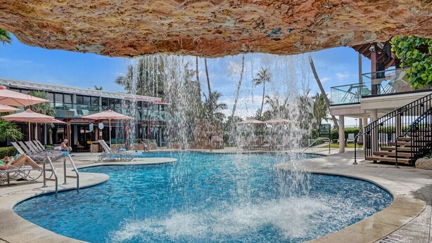 A pool area with a circular pool, lounge chairs, and a waterfall feature. - Chic Coastal Getaway Steps to the Beach with Resort Amenities, Pools, Sauna & Gym 708 (Miami Beach)