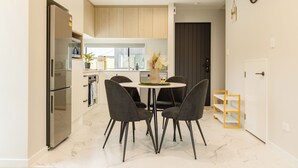 A modern kitchen with a dining area, featuring a marble floor, dark chairs, and a small round table with a vase. - Brand New 3BR Home with Parking in Christchurch (Tristate)