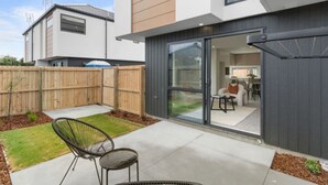 A modern house with a patio, a sliding glass door leading to a living area, and a wooden fence. - Brand New 3BR Home with Parking in Christchurch (Tristate)