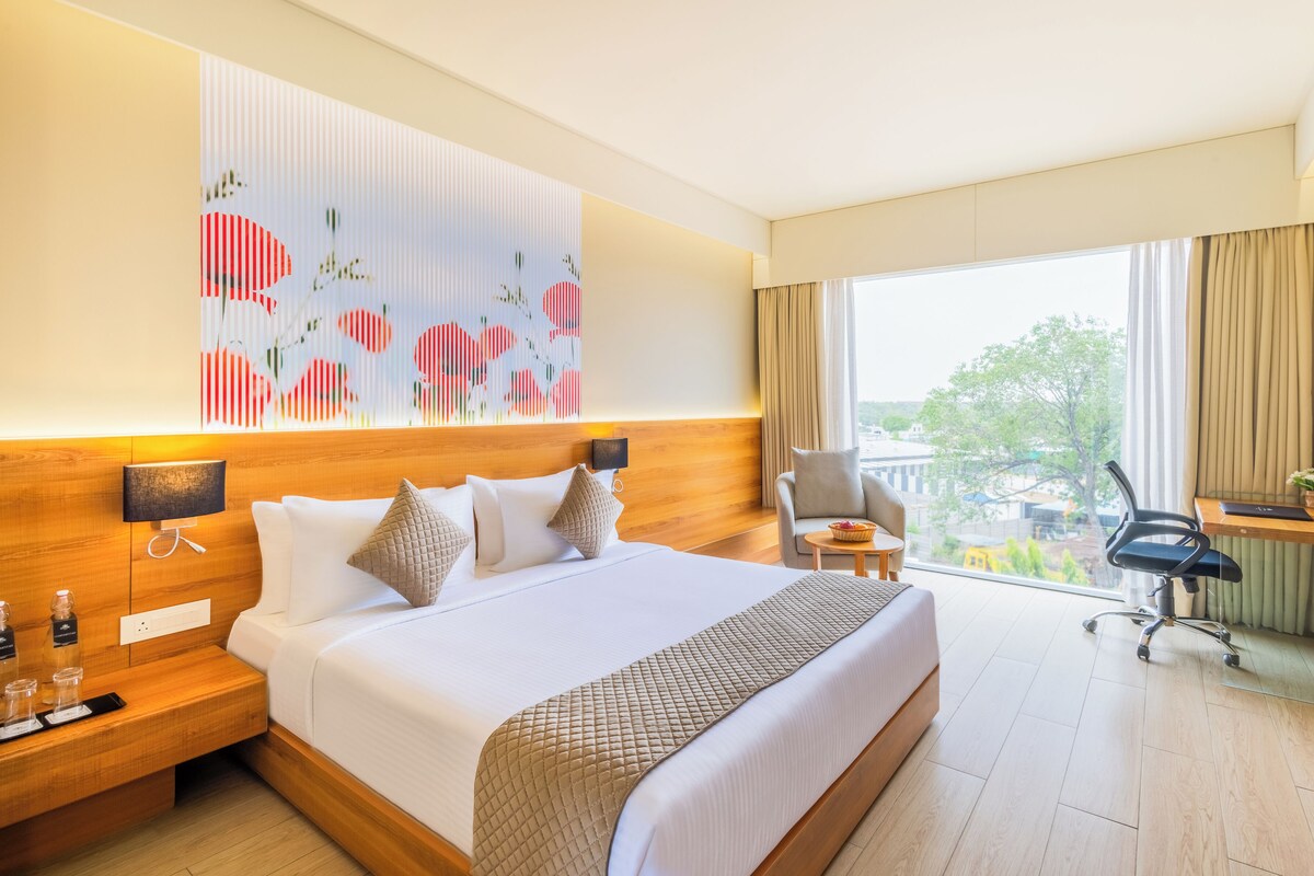 Habitación de hotel con una cama grande, un escritorio, una silla y vistas al exterior.