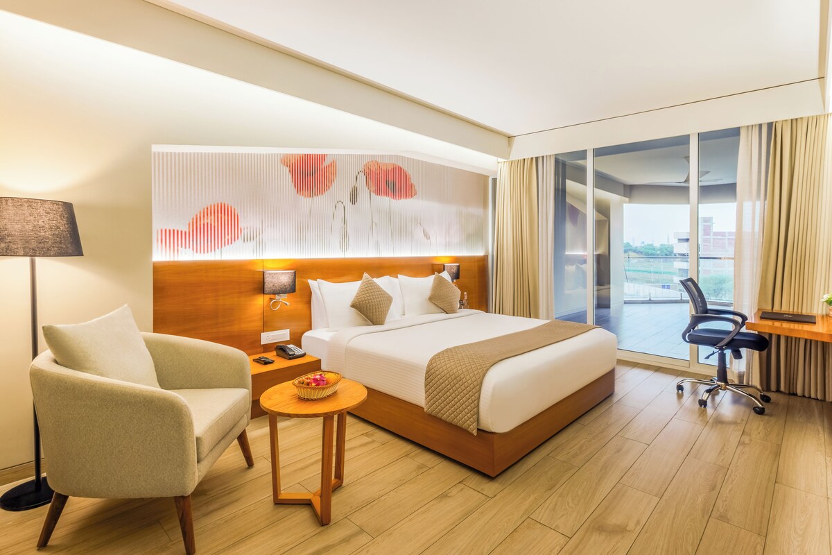 Habitación de hotel moderna con una cama grande, un escritorio, una silla, una lámpara y vistas a la ciudad.