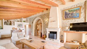 A cozy living room with a fireplace, wooden beams, a television, and a stone wall. - Ses Cases Noves by Rentallorca (Maria de la salut)