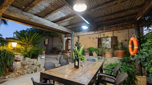An outdoor patio with a wooden table and wicker chairs, surrounded by potted plants and a stone wall. - Ses Cases Noves by Rentallorca (Maria de la salut)
