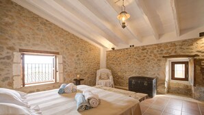 A bedroom with stone walls, a bed with rolled towels, a chair, and a chest of drawers. - Ses Cases Noves by Rentallorca (Maria de la salut)