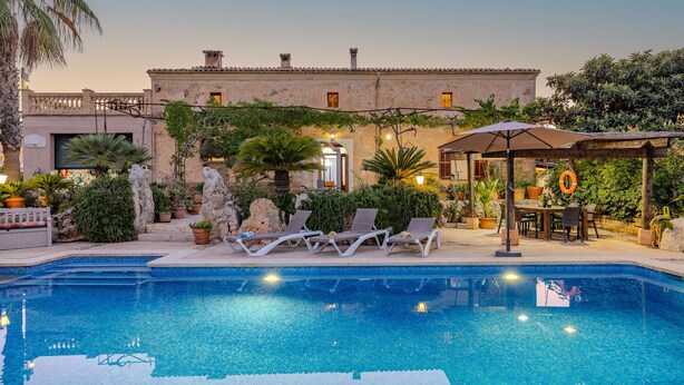 A swimming pool with lounge chairs and a covered seating area, surrounded by potted plants and a building with a tiled roof. - Ses Cases Noves by Rentallorca (Maria de la salut)