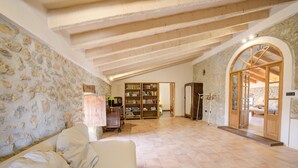 A spacious living room with a high ceiling, exposed beams, a stone wall, and a large bookshelf. - Ses Cases Noves by Rentallorca (Maria de la salut)