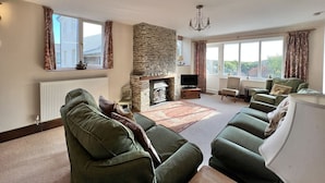 A spacious living room with a stone fireplace, comfortable seating, and large windows. - Coach House Quiet Country Retreat for 6 Near Coast (Loddiswell)