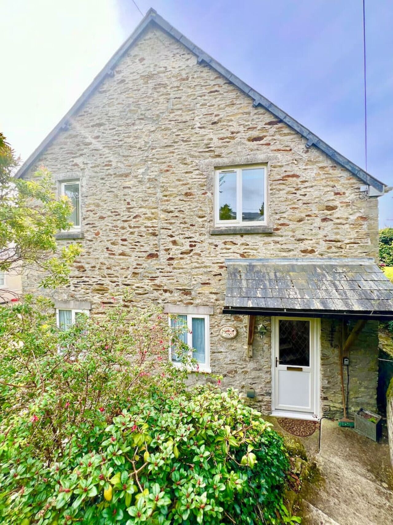 Une maison en pierre avec un toit en pente, un petit porche et une fenêtre.