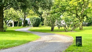 A curved road in a park-like setting with a sign indicating a 'Conch House' and 'Wild Stream Terrace'. - Coach House Quiet Country Retreat for 6 Near Coast (Loddiswell)