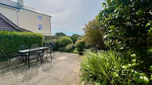 A patio with a table and chairs, surrounded by lush greenery and a house in the background. - Coach House Quiet Country Retreat for 6 Near Coast (Loddiswell)