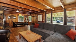 A cozy cabin interior with a wooden ceiling, a gray sofa, a wooden table, and a stone wall. - Sunshine Cabin Cozy 2-Story Getaway (Big Bear Lake)
