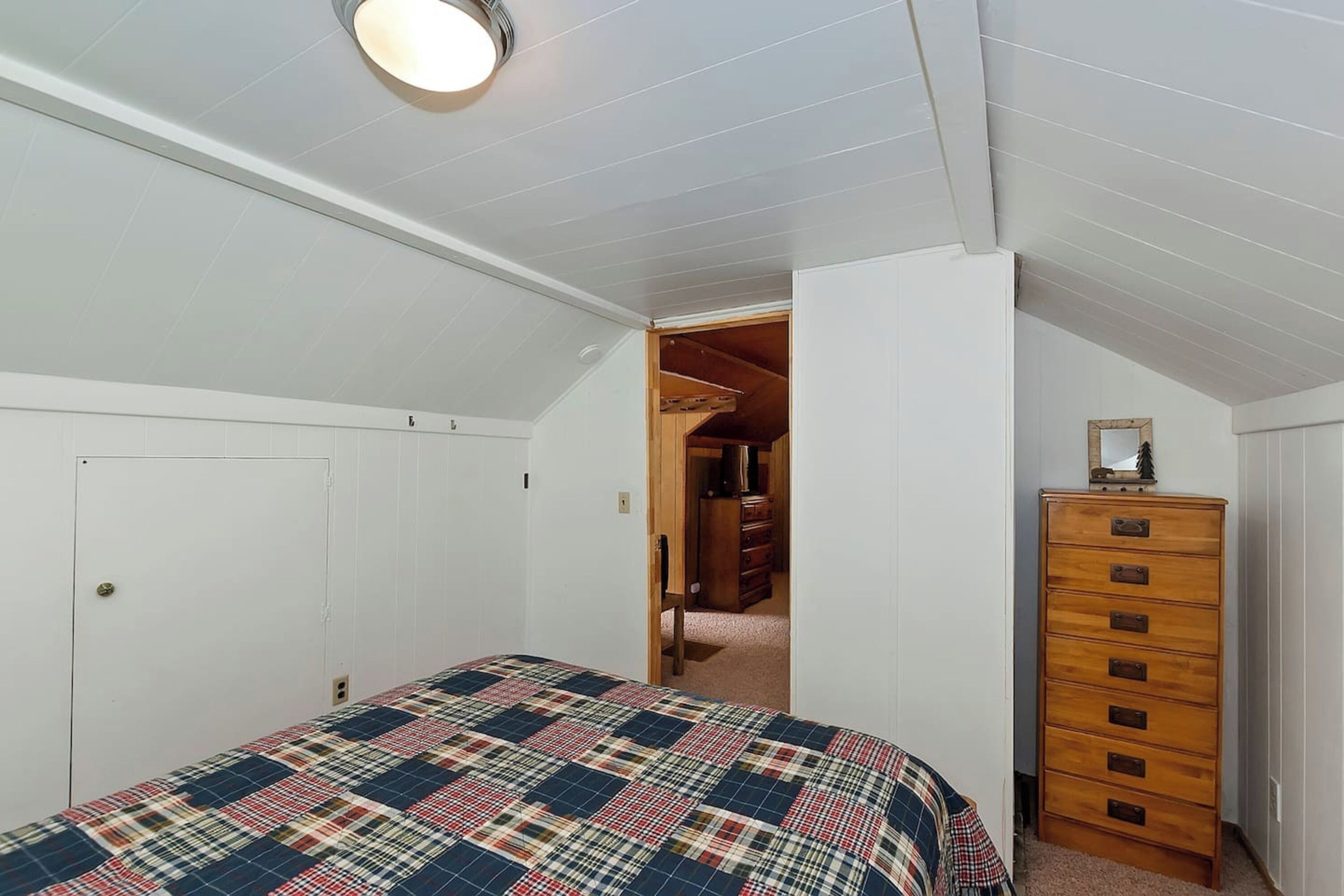 Een slaapkamer met een bed, een dressoir en een deur die naar een gang leidt.