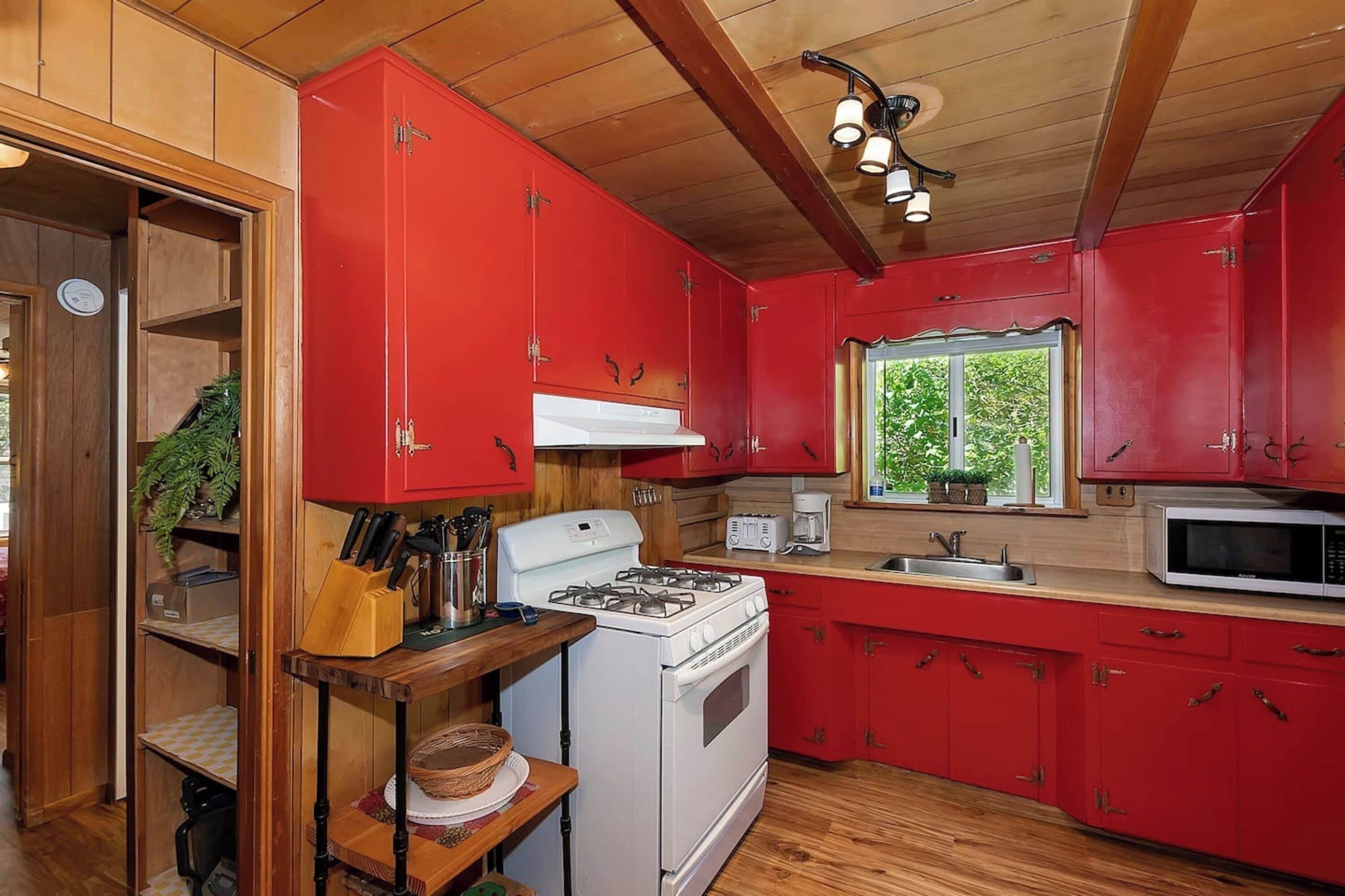 Une cuisine avec des meubles de couleur rouge, une cuisinière blanche et un four à micro-ondes.