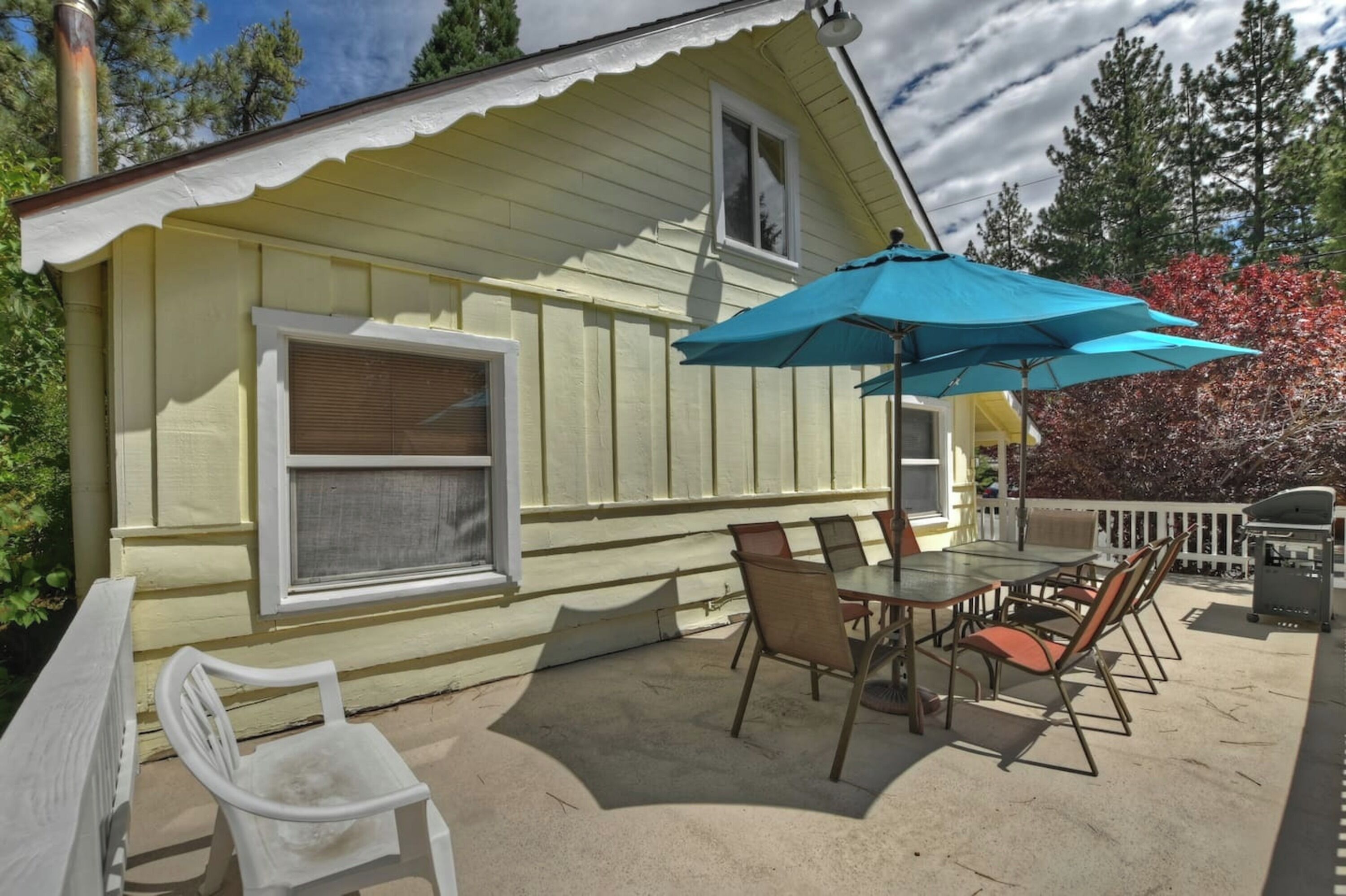 A yellow house with a covered patio, a table with chairs, and a grill.