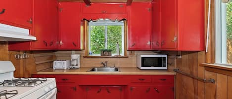 Una cocina compacta con armarios rojos, estufa blanca, microondas y ventana con vistas al verdor.