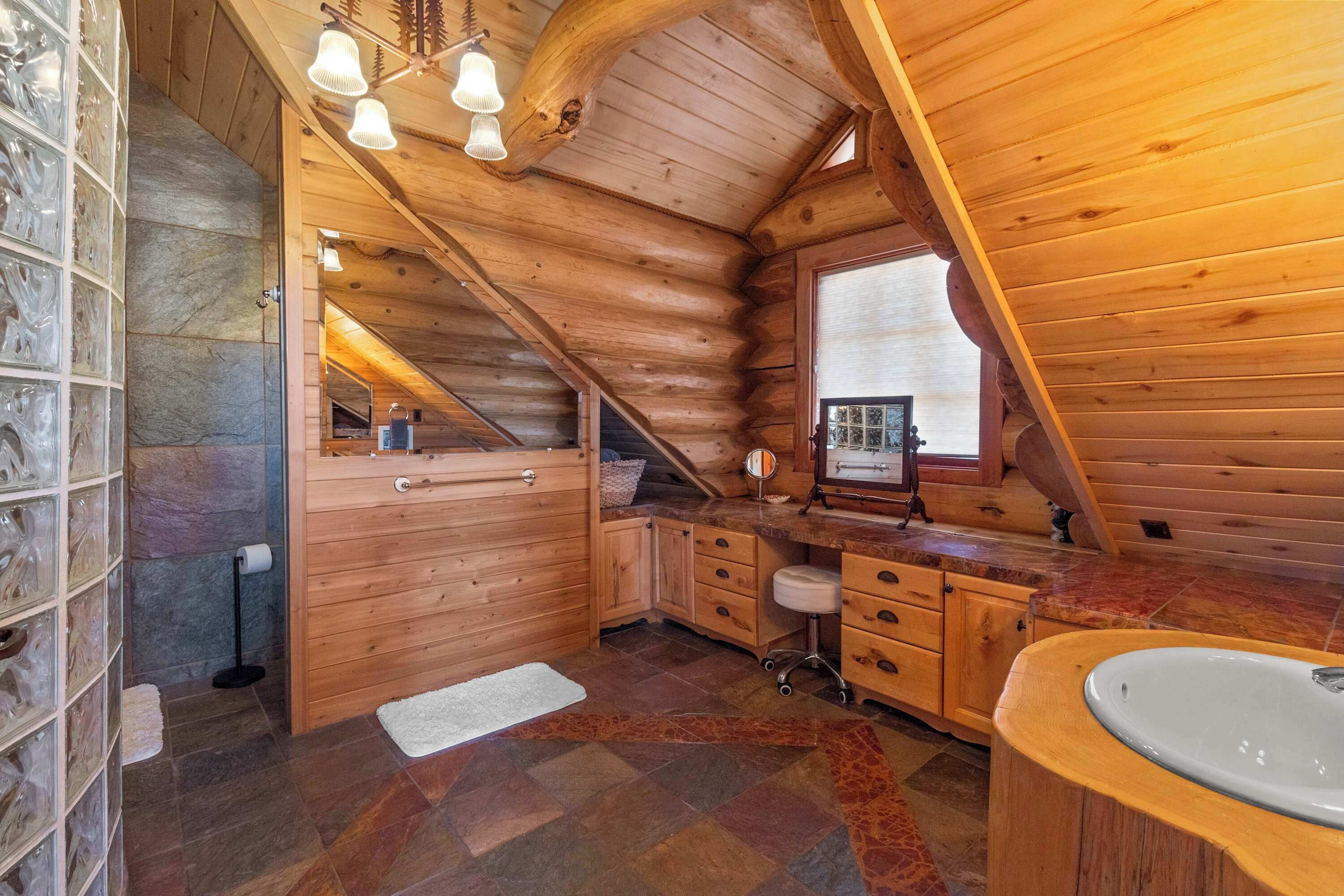 Ein Badezimmer in einer Blockhütte mit Steinwand, Holzschränken, einem Waschbecken und einem Spiegel.