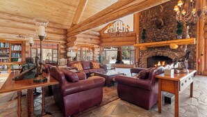 A log cabin interior with a stone fireplace, leather sofas, and a chandelier. - Legacy Lodge & Barn Retreat, Sleeps 42 (Heber)